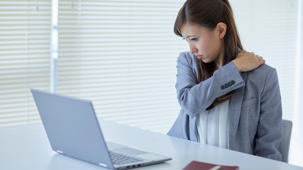 パソコンの前に座って肩を押さえておる姿